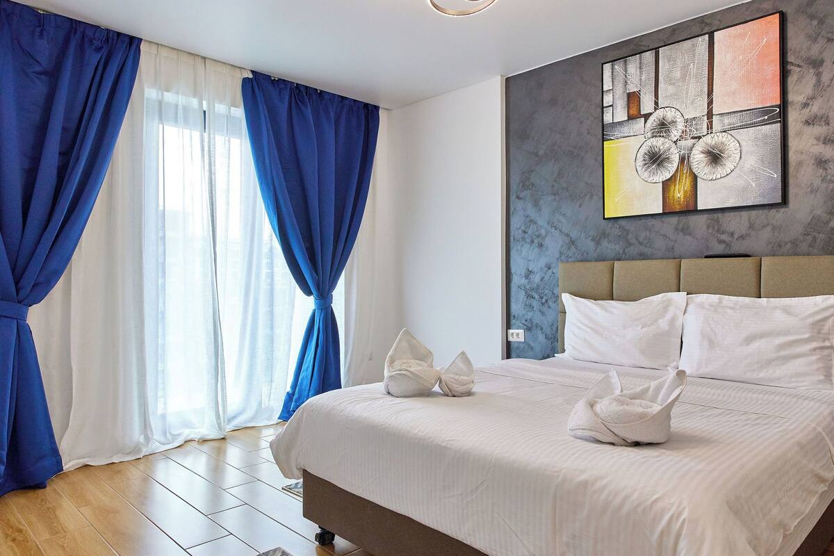 A hotel room with a large bed, white bedding, and a painting on the wall.