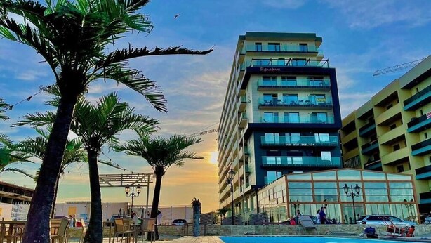 A modern hotel with a pool, palm trees, and a multi-story building with balconies. - Dream Mamaia North (Navodari)