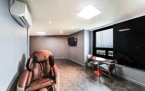 A modern room with a massage chair, a small table, and a TV mounted on the wall.