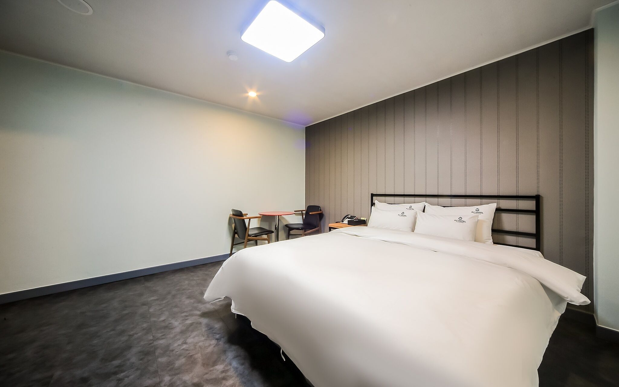 A hotel room with a large bed, a desk, a chair, and a small table.