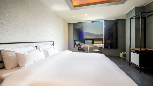 Habitación de hotel moderna con una cama grande, un escritorio y vistas a montañas a través de un ventanal amplio.