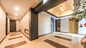 Un corredor de hotel moderno con un diseño limpio y minimalista, que presenta un camino recto con flechas direccionales en el suelo, un techo con iluminación empotrada y un amplio ventanal a la derecha.
