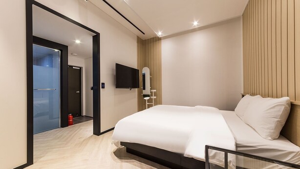 Une chambre d’hôtel moderne dotée d’un grand lit, d’un téléviseur à écran plat fixé au mur et d’un panneau décoratif en bois sur le mur.