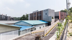 Un hôtel moderne avec un toit bleu, une enseigne indiquant « BRAVO HOTEL » et un parking clôturé.