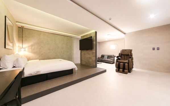 Ein modernes Hotelzimmer mit Bett, Massagesessel, einer Couch und einem flachbildfernseher an der Wand.