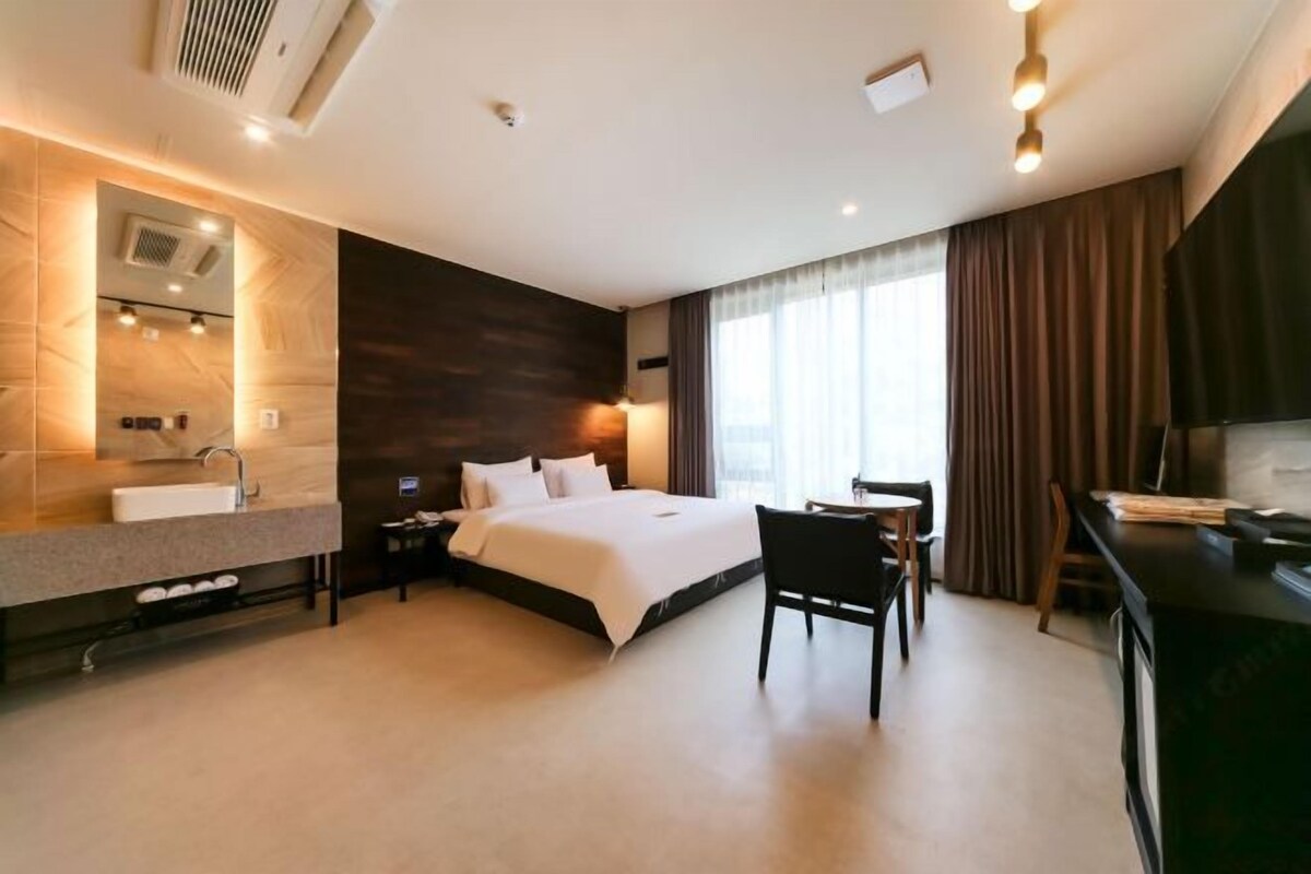 Een moderne hotelkamer met een groot bed, een bureau, een stoel, een kaptafel met spiegel en een televisie.