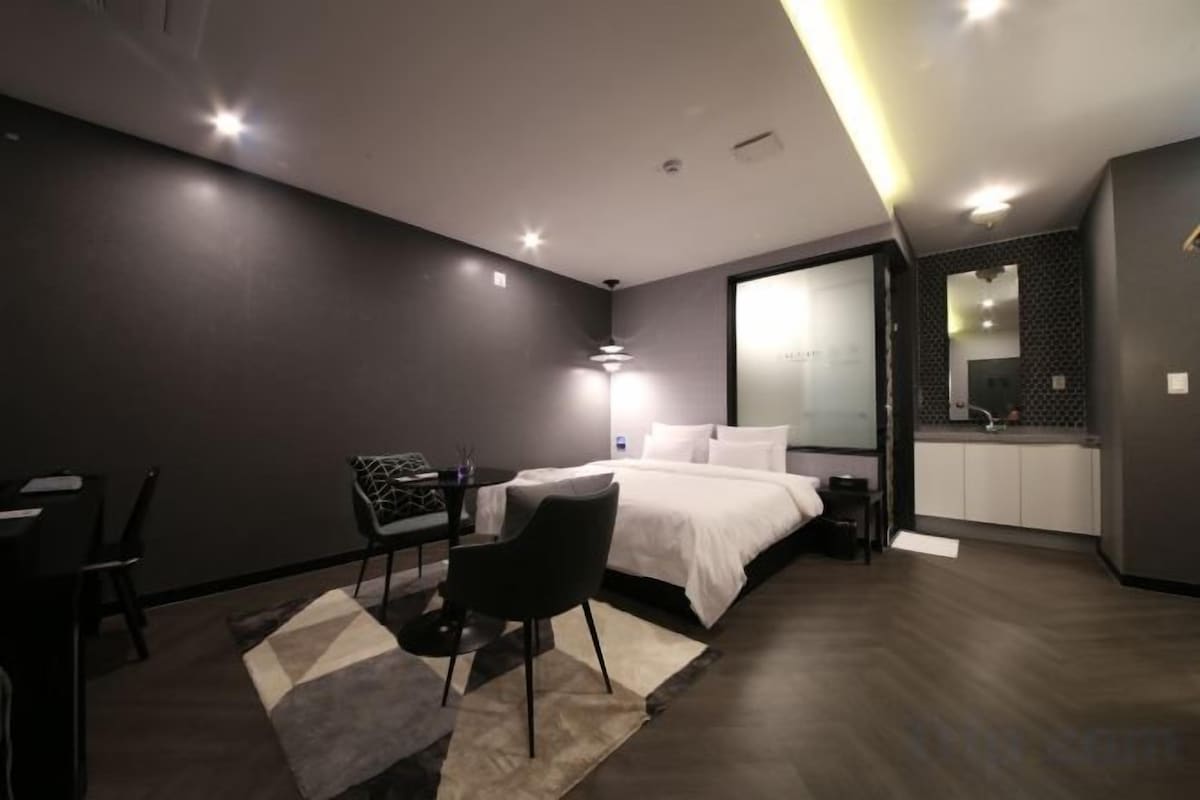 Een moderne hotelkamer met een bed, bureau, stoel en uitzicht op de keuken.