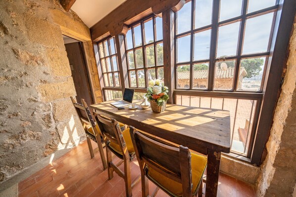A rustic dining area with a wooden table and chairs, large windows, and a view of the outside.