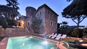 A swimming pool with a stone edge, surrounded by lounge chairs and a stone building with arched windows. - Can Xirau Castle | Private Pool Sea Views Air Conditioning Ideal Families (SANTA SUSSANA)