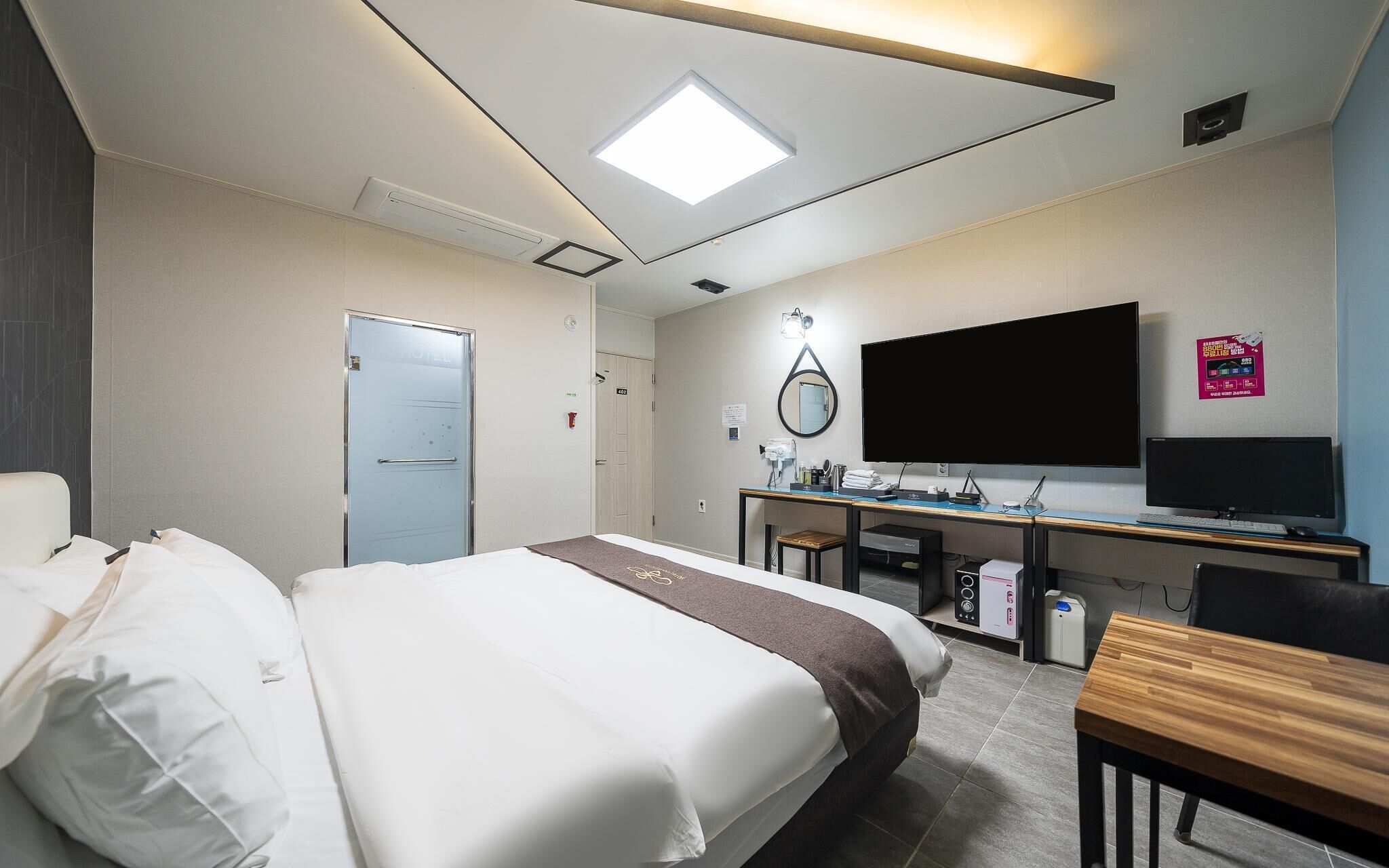 A hotel room with a bed, desk, television, and a door.