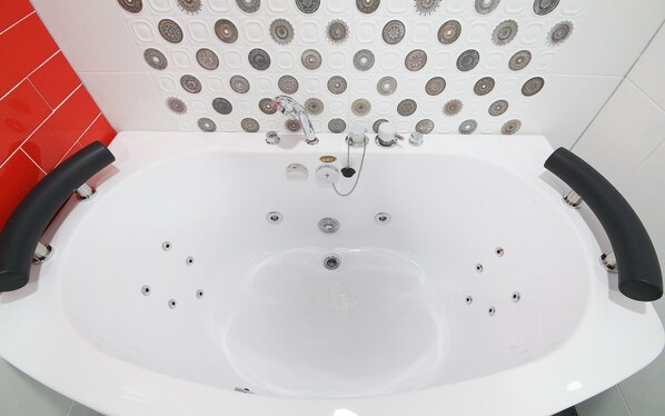 A white bathtub with two black handles, a tiled wall with decorative plates, and a red tiled section on the left.