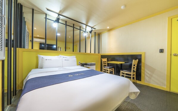 A hotel room with a bed, a small table with two chairs, a mirror, and a yellow door. - Cheonan E (Cheonan)