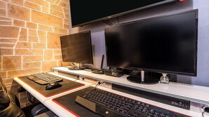 A computer setup with two monitors, a keyboard, and a mouse on a desk against a brick wall. - Cheonan E (Cheonan)