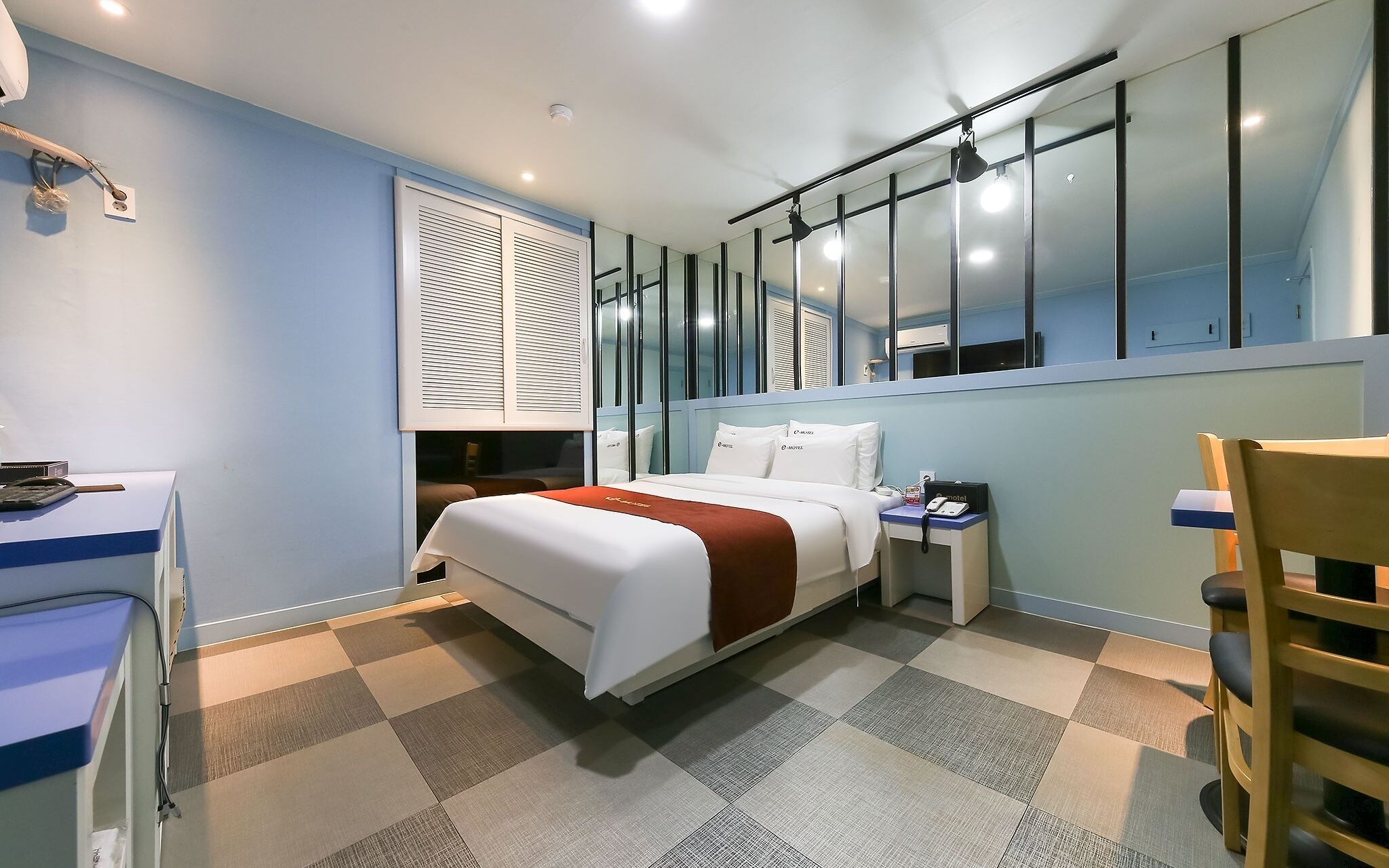 A hotel room with a bed, a desk, a chair, and a large mirror.