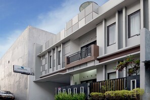 Un edificio moderno con un letrero que indica D'Paragon Guesthouse. Cuenta con un balcón con barandilla, una entrada con reja y plantas en macetas.