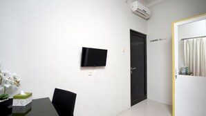 A hotel room with a flat-screen TV mounted on the wall, a black door, and a white-framed mirror with a curtain. - Dparagon Pamela 1 (Depok)