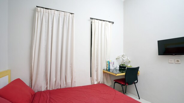 A hotel room with a bed, a desk with a chair, a television, and curtains. - Dparagon Pamela 1 (Depok)