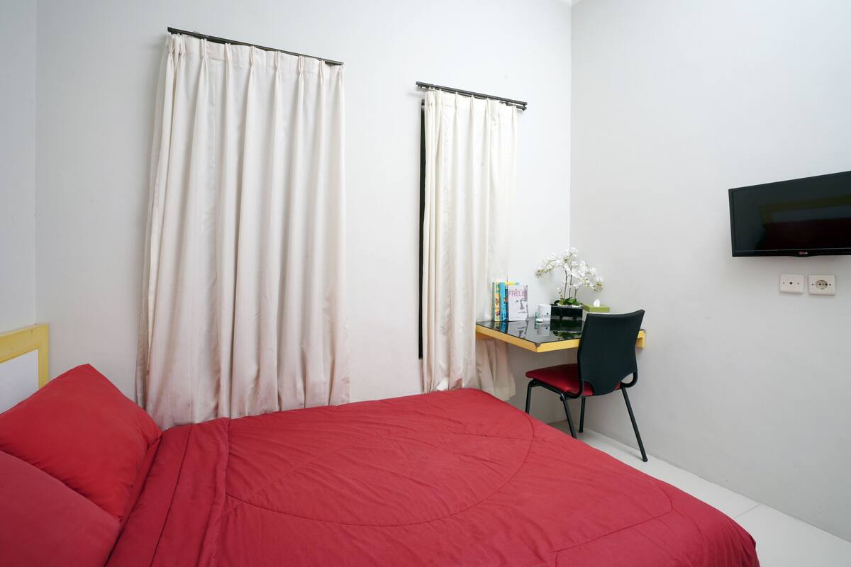 A hotel room with a bed, a desk with a chair, a television, and curtains.