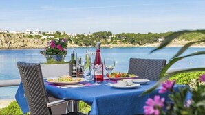 Ein Tisch ist für das Essen gedeckt, mit Blick auf das Meer und die Hügel im Hintergrund.