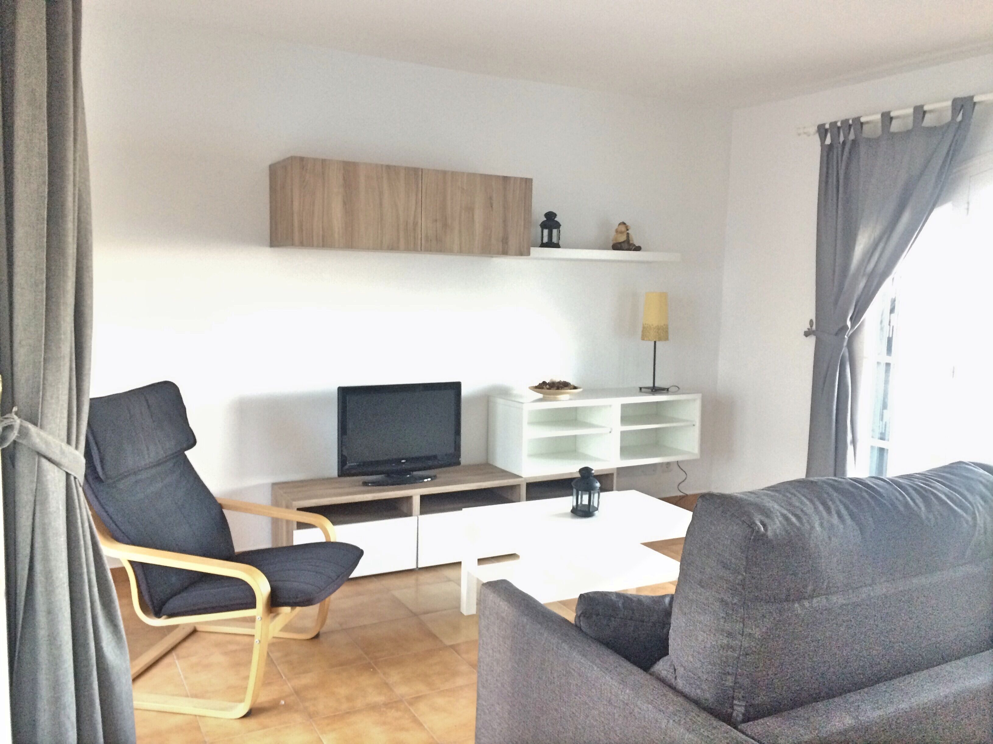 A modern living room with a flat-screen TV, a white coffee table, and two grey sofas.