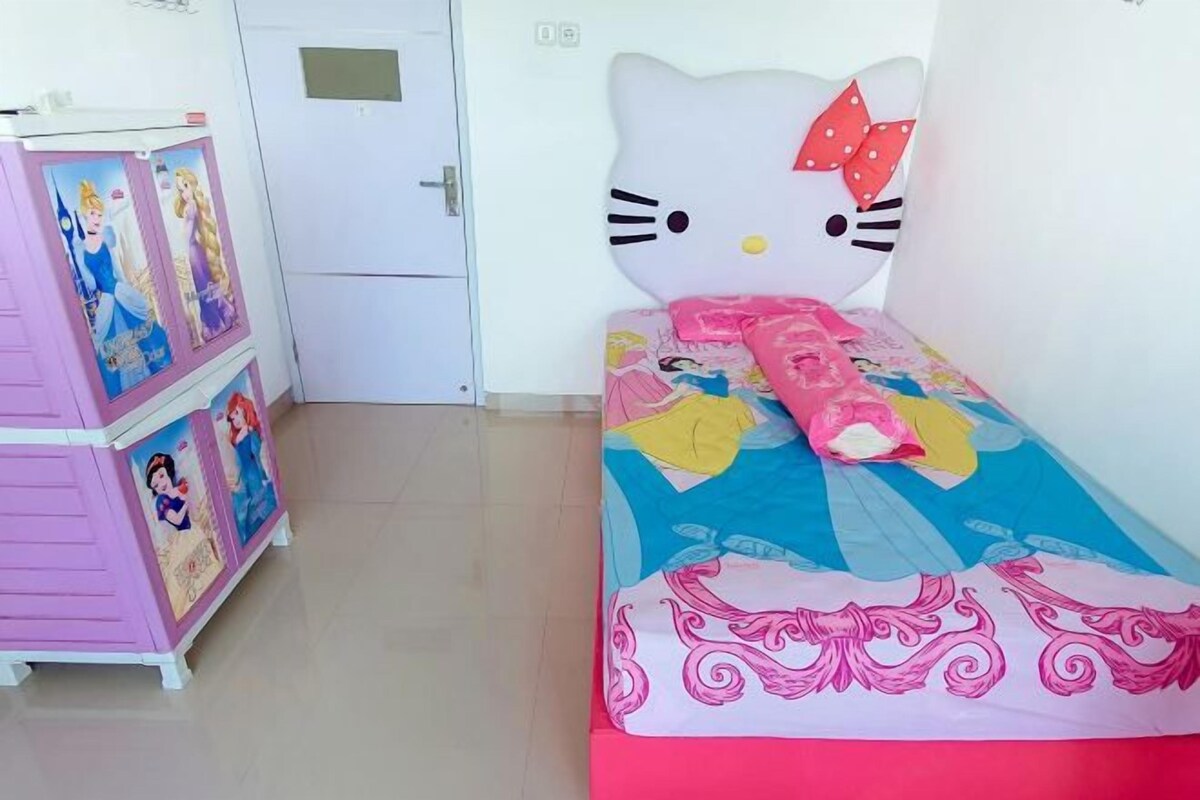 A child's bedroom with a Hello Kitty headboard, a pink dresser with Disney princess posters, and a bed with a colorful bedspread.