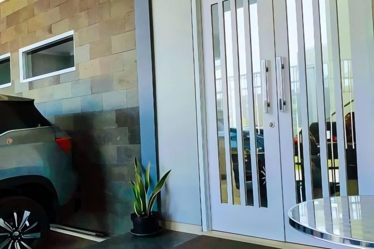 A modern building entrance with a car parked outside, a potted plant, and a glass door with vertical bars.