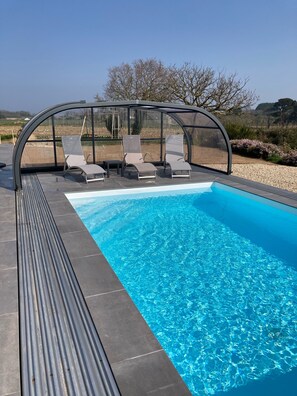 Une piscine dotée d’une enceinte en verre, trois chaises longues et une vue sur le paysage environnant.