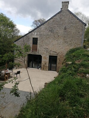 A stone building with a large patio area, outdoor seating, and a view of the surrounding landscape. - Grande Propriété le Long du Ruisseau (ST NOLFF)