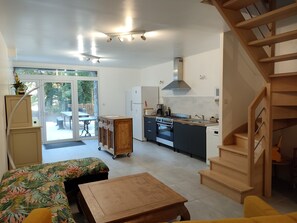 A modern kitchen with a built-in oven, a microwave, and a sink. There is a wooden staircase to the right and a sliding glass door leading to an outdoor area. - Grande Propriété le Long du Ruisseau (ST NOLFF)