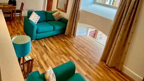 Una sala de estar con un sofá verde, una mesita y una ventana con cortinas.