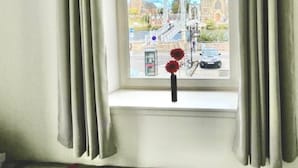 Una habitación con cama, ventana con cortinas y vista a un paisaje urbano que incluye una iglesia y un puente.