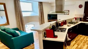 Una cocina moderna con una isla central, suelo de madera y un sofá color turquesa en la sala.