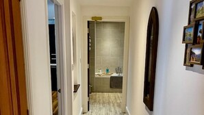 Un pasillo con piso de madera, un radiador blanco y una puerta que da a un baño con ducha azulejada.