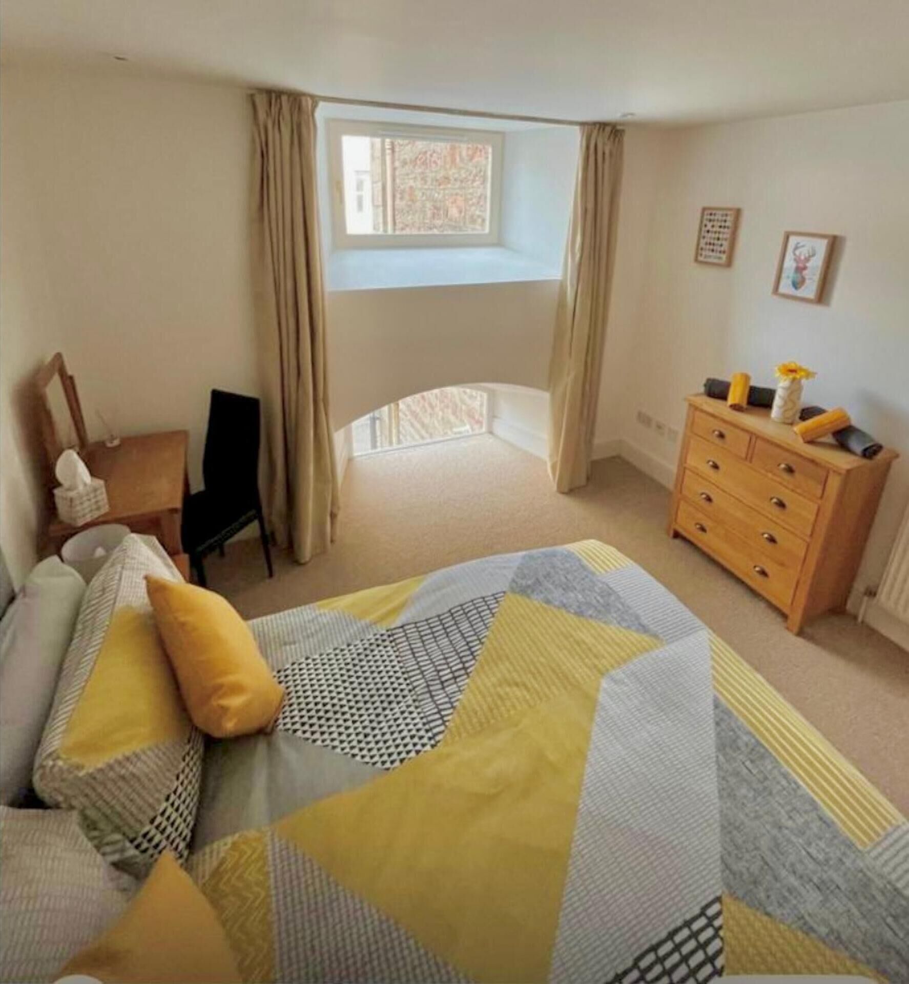 A bedroom with a bed, a dresser, a window with curtains, and a chair.