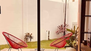 A patio area with two red wicker chairs, a small round table, and potted plants.