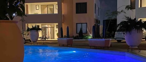 Un edificio moderno con piscina, plantas en macetas y una entrada bien iluminada.