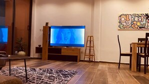 A modern living room with a large flat-screen TV, wooden flooring, a patterned rug, and a minimalist art piece on the wall.