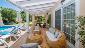 Un espacio al aire libre techado con mobiliario de mimbre, piscina y una mesa de patio.