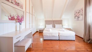 Un dormitorio con dos camas, un aparador, una mesita de noche y una repisa con flores.