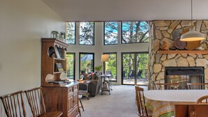 Amplia sala de estar con chimenea de piedra, ventanas grandes y mesa de comedor con sillas.