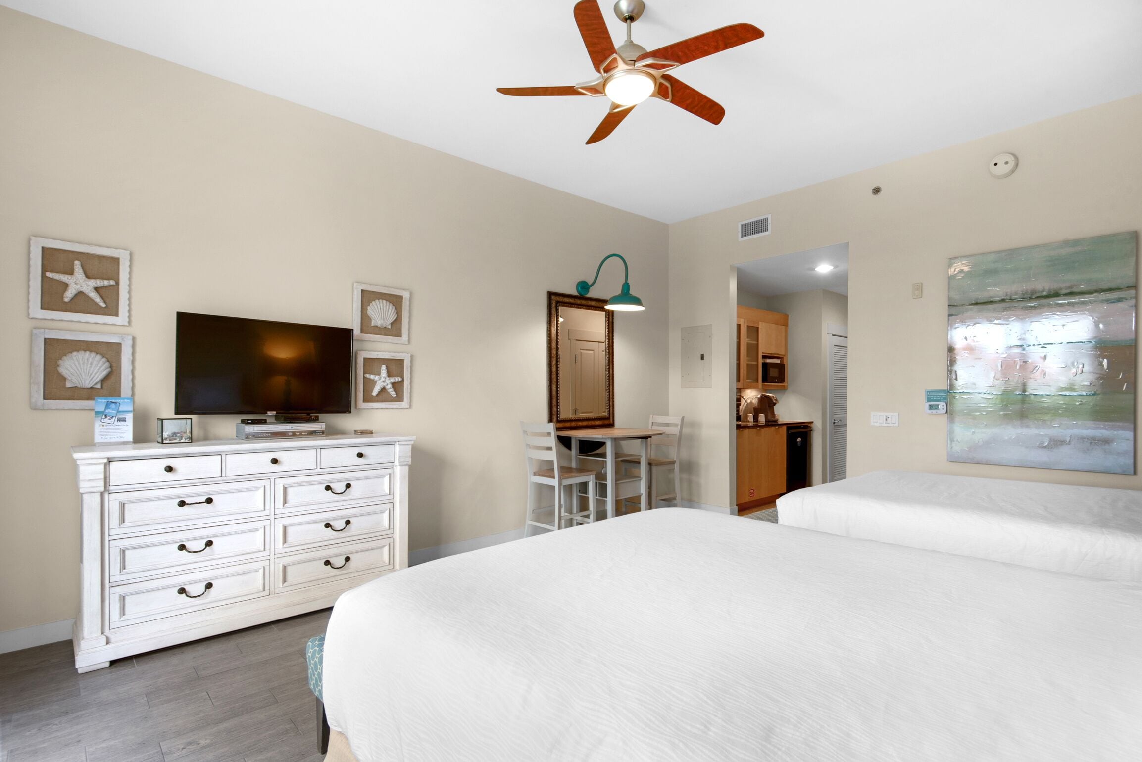 Une chambre d’hôtel équipée d’un lit, d’une télévision, d’une commode, d’un bureau et d’un ventilateur de plafond.