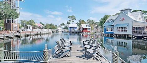 A wooden dock with chairs and a rope barrier over a calm water body, surrounded by buildings with distinct architectural styles.