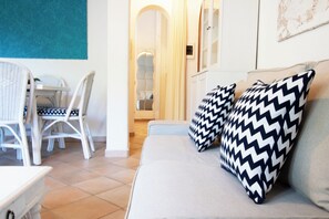A modern living room with a sofa, patterned pillows, a dining area with chairs, and a view of the hallway. - La Scalinatella - Private apartment with Sea View (Forio)