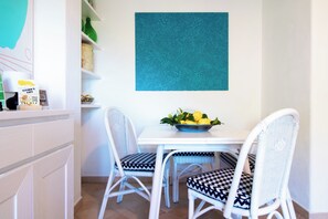A dining area with a white table, two chairs with patterned cushions, a bowl of lemons, and a blue textured wall. - La Scalinatella - Private apartment with Sea View (Forio)