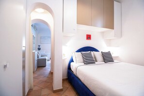 Camera d'albergo con un letto, un comodino, una mensola a parete e un bagno visibile attraverso un arco.