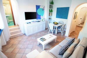 Un soggiorno moderno con una TV a schermo piatto, un'area pranzo con tavolo e sedie, e una scala che conduce a un piano superiore.