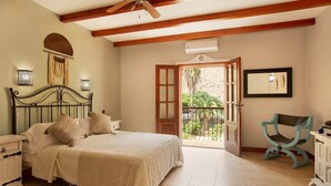 Ein Schlafzimmer mit Bett, Nachttisch, Kommode, Stuhl und einem Balkon mit Blick auf Grünflächen.