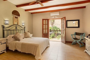A bedroom with a bed, a nightstand, a dresser, a chair, and a balcony with a view of greenery.