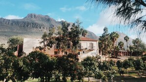 Ein Gebäude mit rotem Ziegeldach, umgeben von viel Grün und einer Bergkulisse.