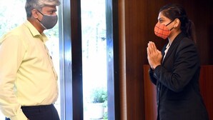 Dos personas frente a una puerta, una con una camisa amarilla y la otra con un traje negro.